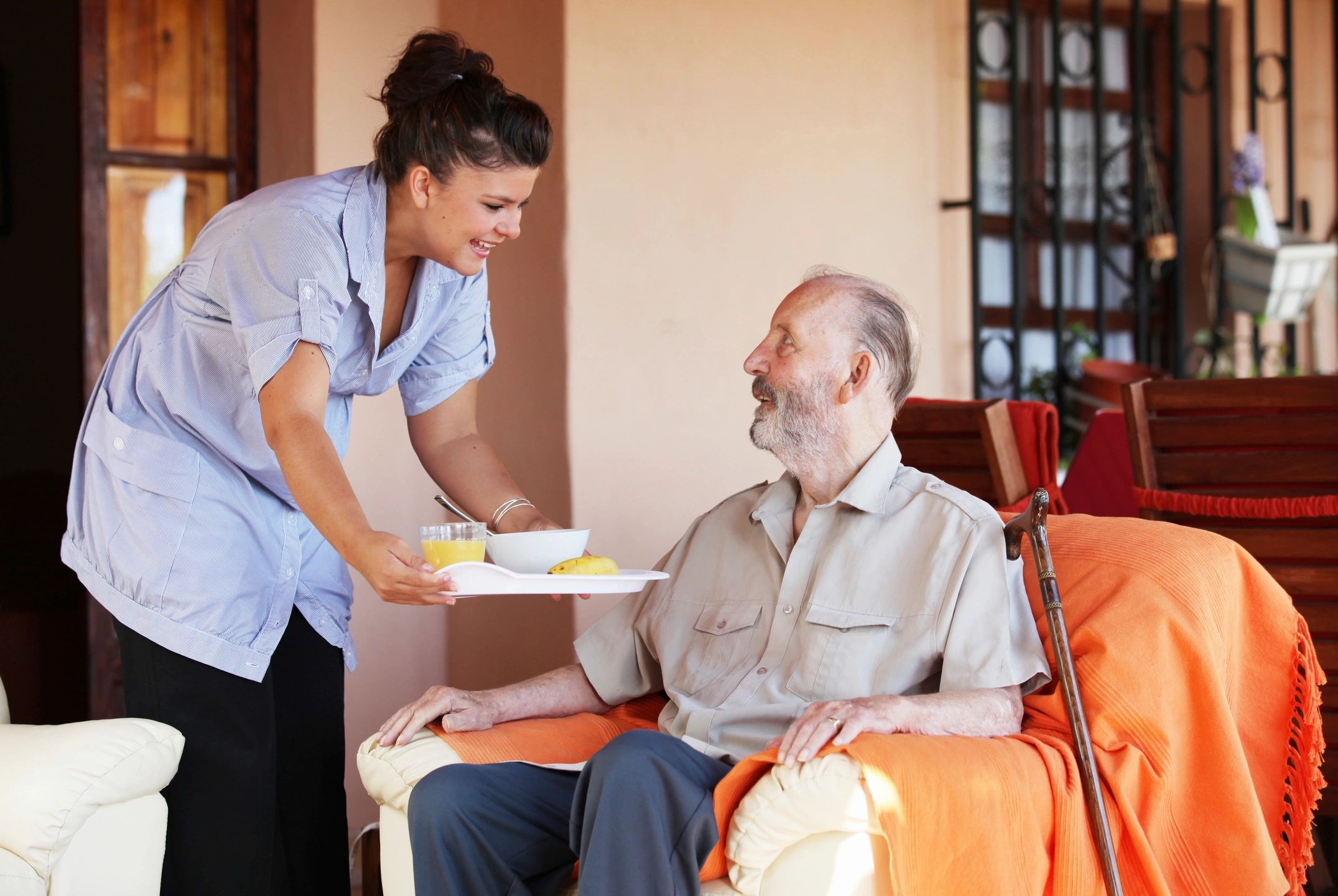 Caregiver serving meal to elderly man at home